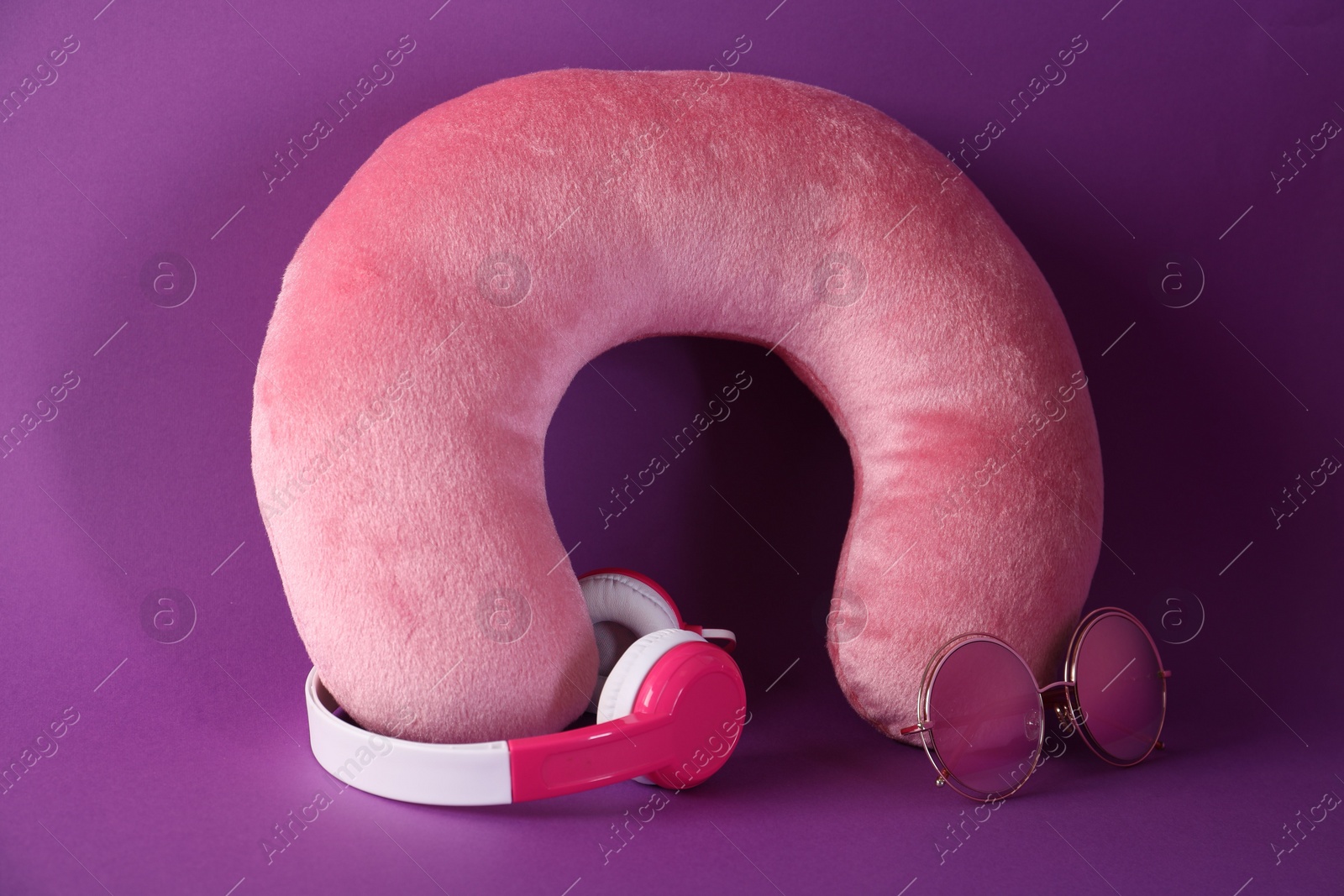 Photo of Pink travel pillow, headphones and sunglasses on violet background