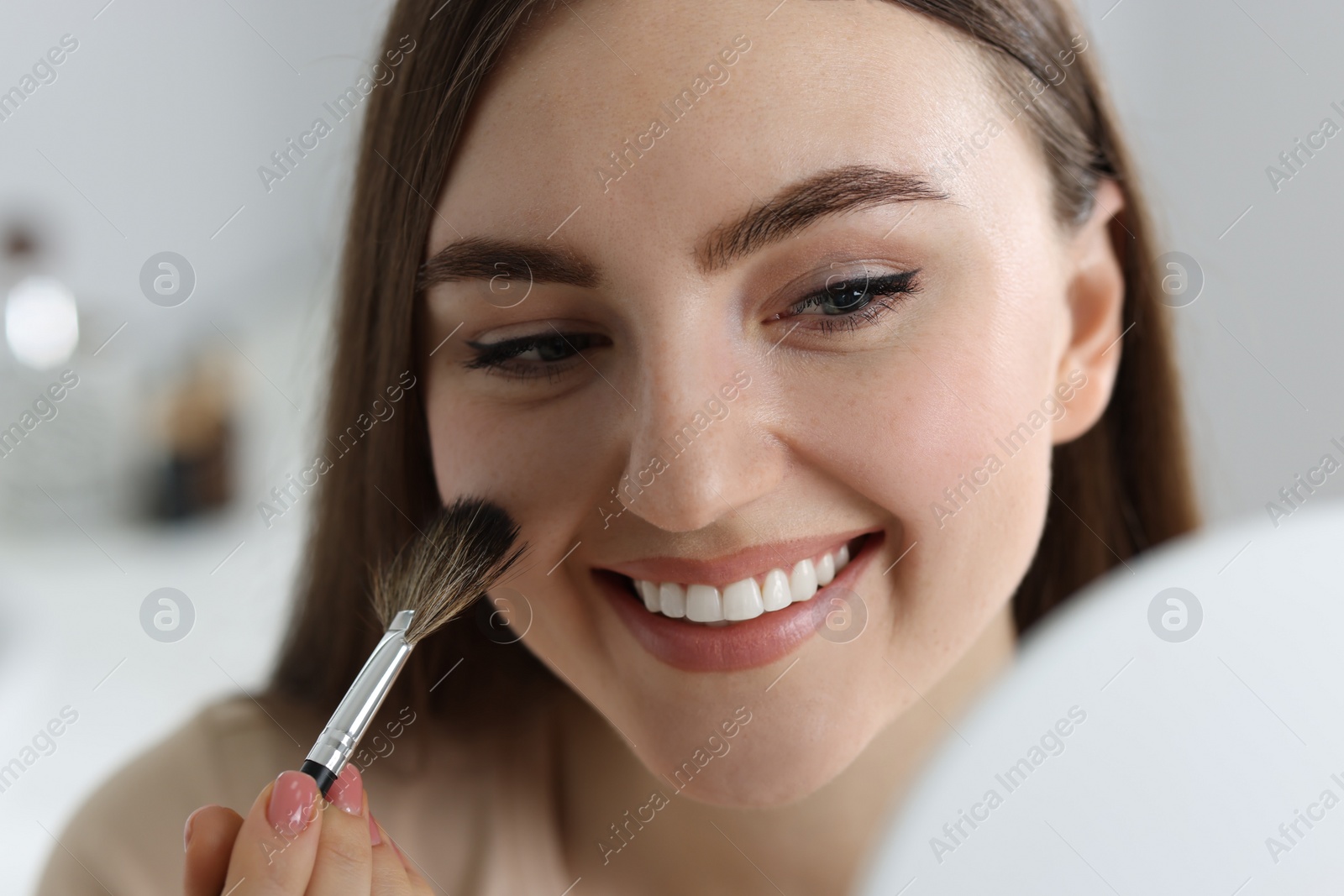 Photo of Smiling woman drawing freckles with brush indoors, closeup
