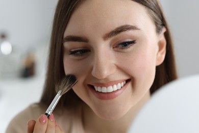 Smiling woman drawing freckles with brush indoors, closeup