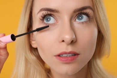 Photo of Beautiful woman applying mascara on orange background, closeup