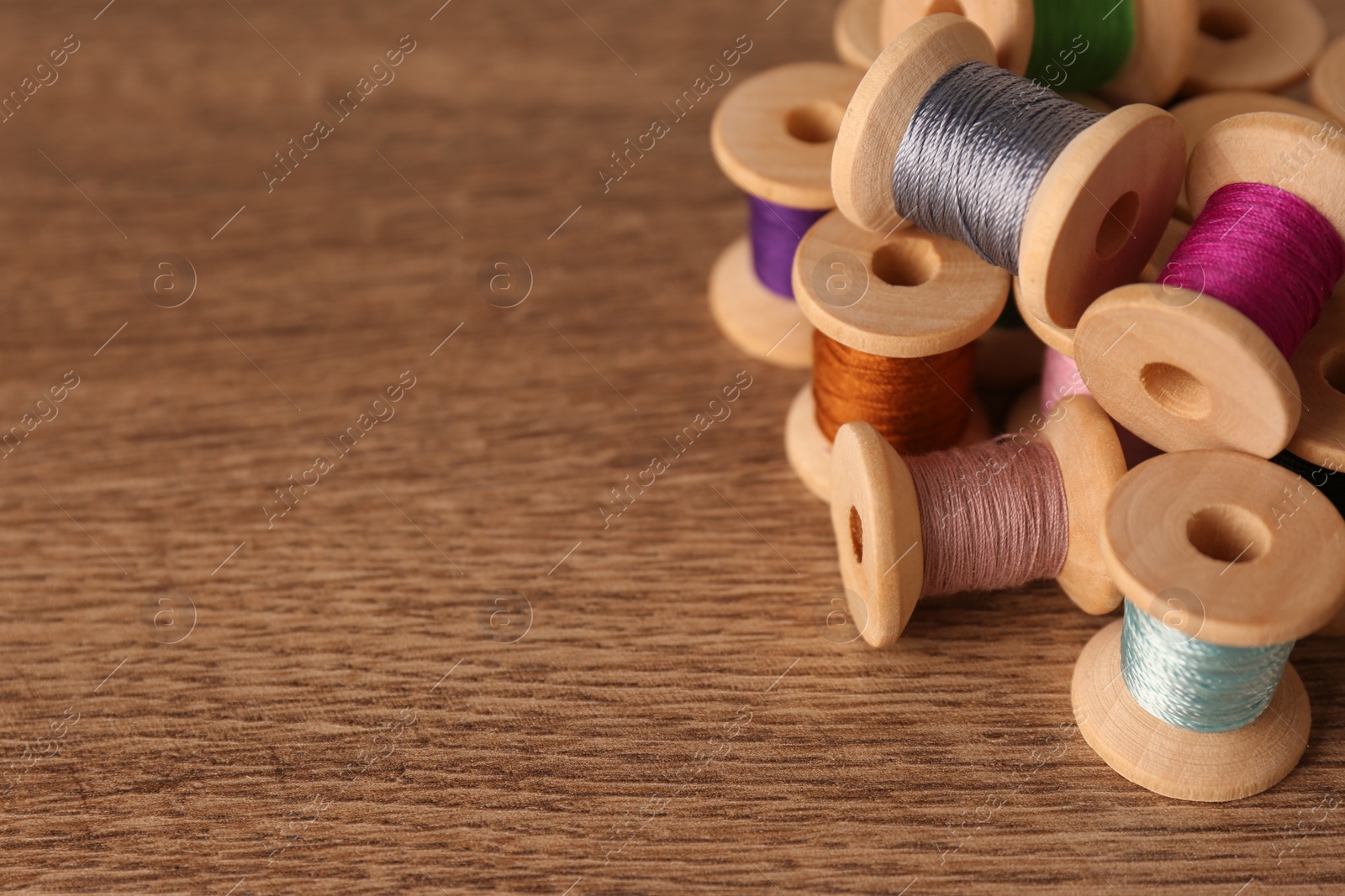 Photo of Set of color sewing threads on wooden table, space for text