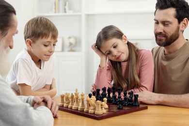 Photo of Family playing chess together at table in room