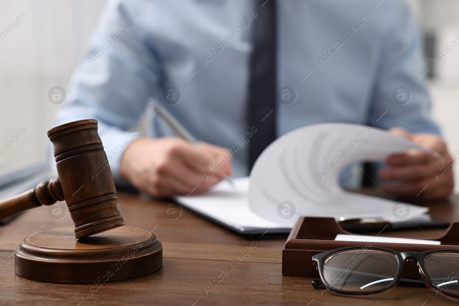 Photo of Lawyer working at wooden table indoors, focus on gavel