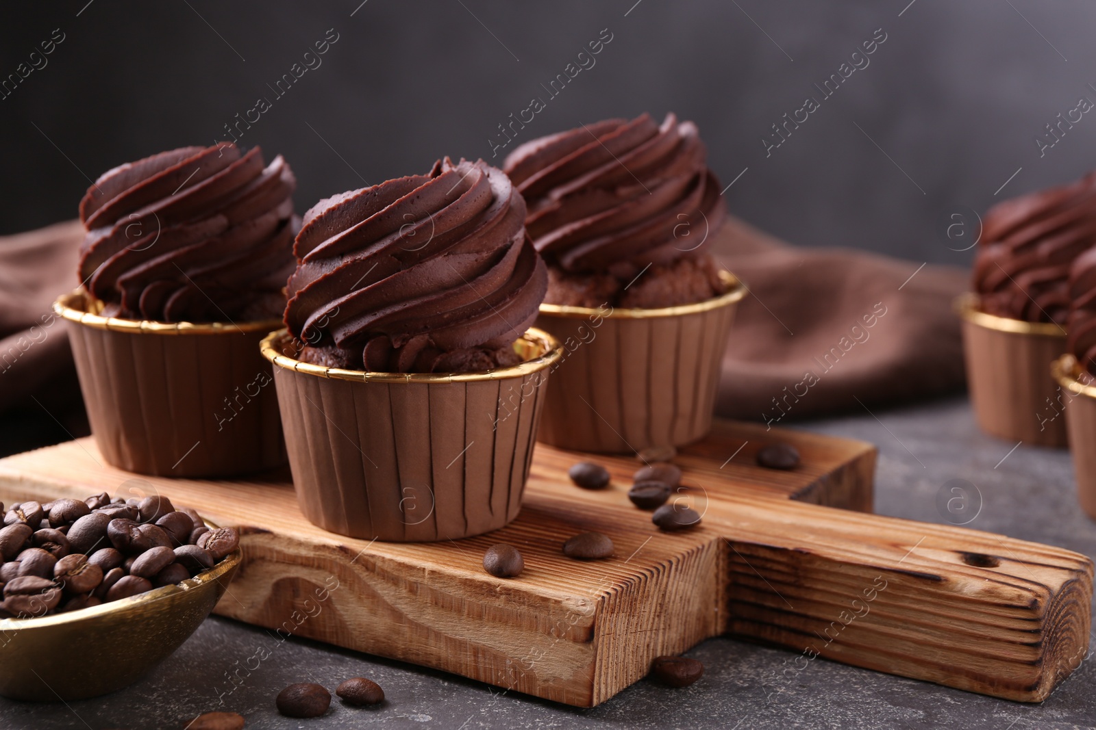 Photo of Delicious chocolate cupcakes and coffee beans on grey textured table, closeup