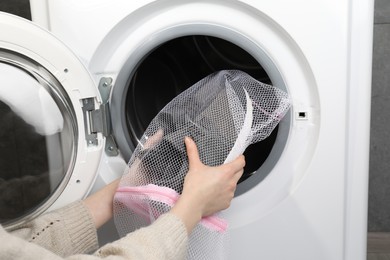 Woman putting stylish sneakers into washing machine, closeup