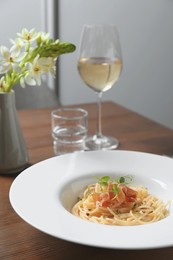 Tasty spaghetti with prosciutto and microgreens served on wooden table, closeup. Exquisite presentation of pasta dish