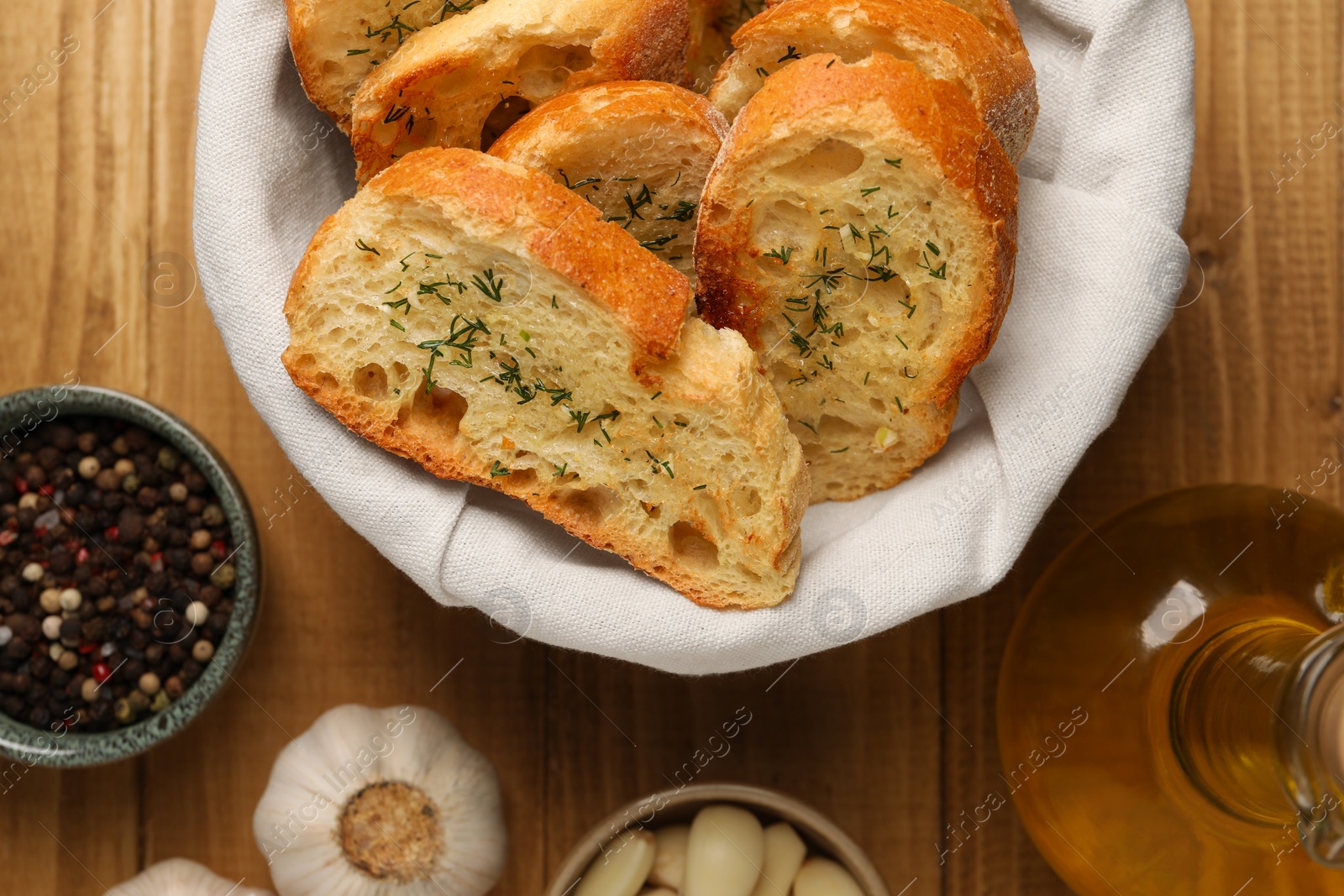 Photo of Tasty baguette with garlic, oil and other spices on wooden table, flat lay