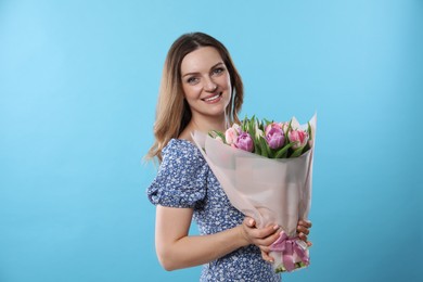 Photo of Happy young woman with bouquet of beautiful tulips on light blue background