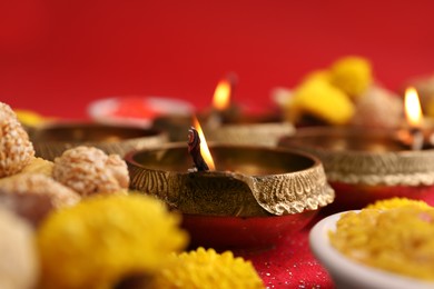 Photo of Diwali celebration. Diya lamps and tasty Indian sweets on shiny red table, closeup