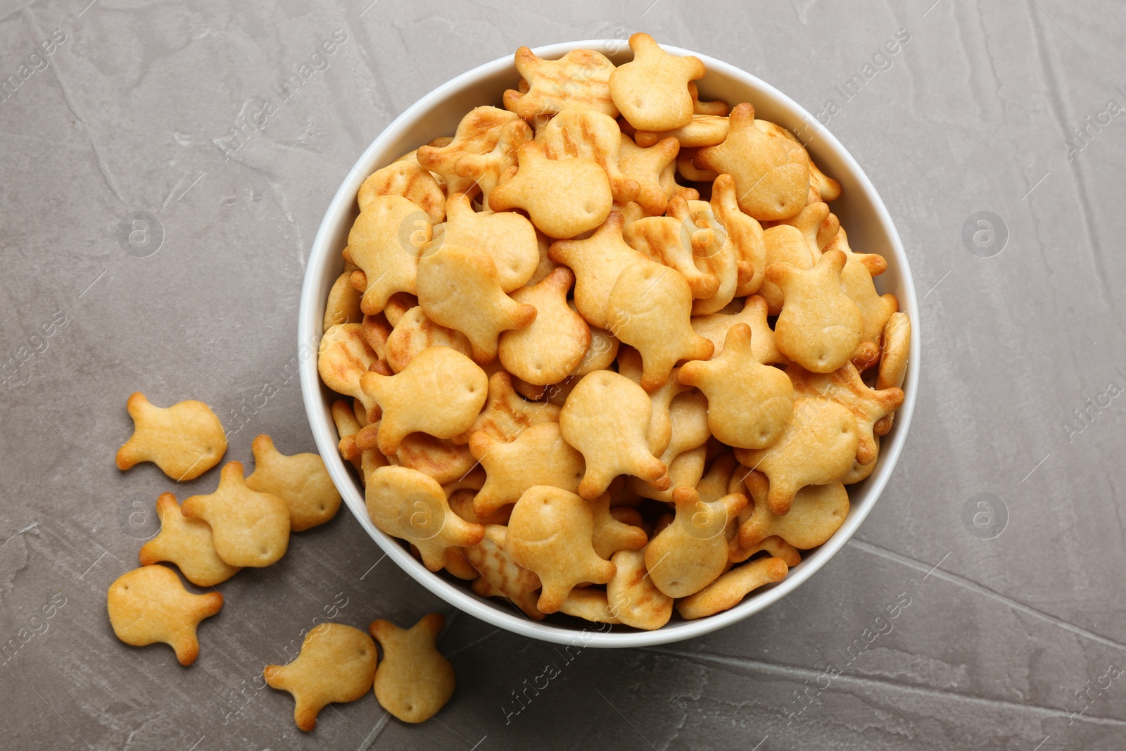 Photo of Delicious goldfish crackers in bowl on grey table, flat lay