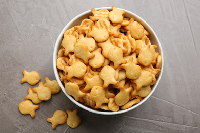 Delicious goldfish crackers in bowl on grey table, flat lay