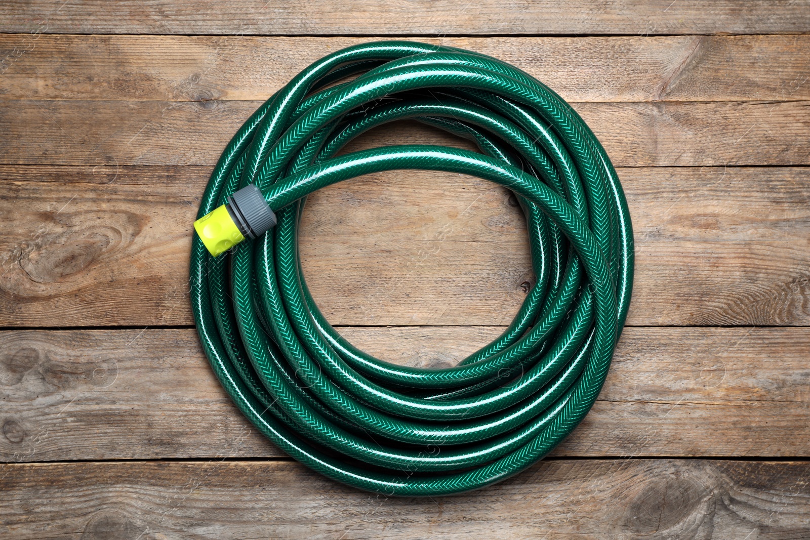 Photo of Green garden hose on wooden table, top view