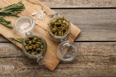 Photo of Delicious pickled capers and rosemary twigs on wooden table, top view. Space for text