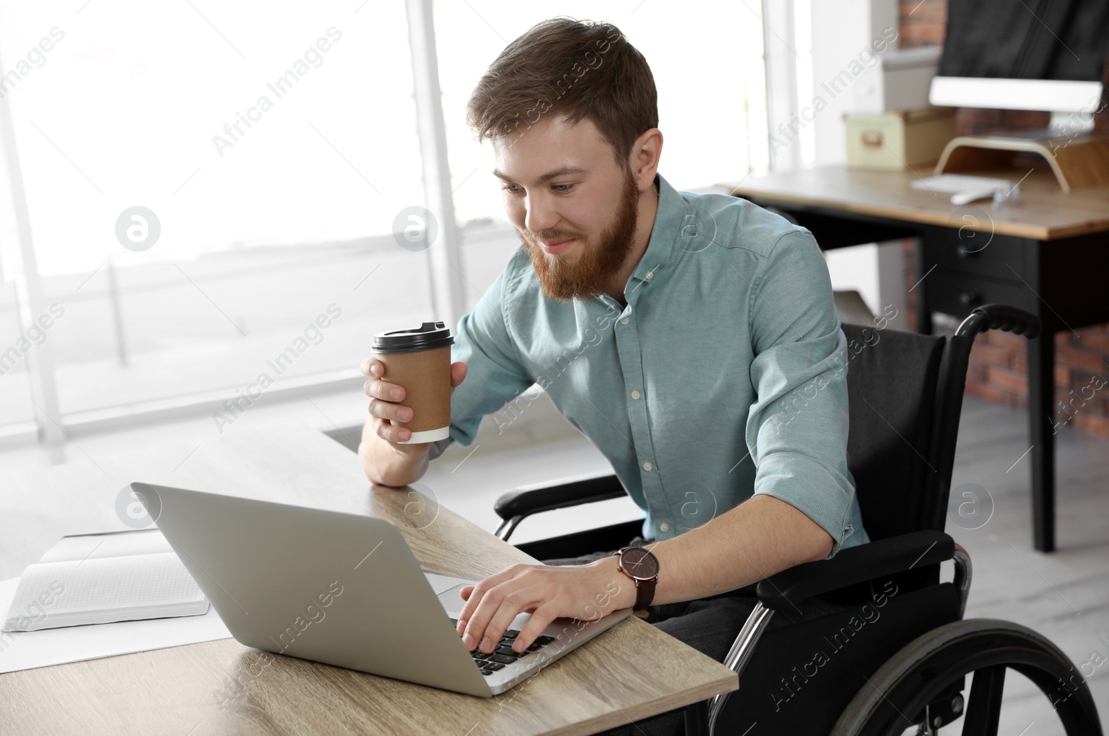 Photo of Young man in wheelchair using laptop at workplace