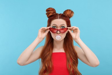 Portrait of beautiful woman in sunglasses blowing bubble gum on light blue background