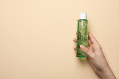 Photo of Woman holding micellar water in bottle on beige background, closeup. Space for text