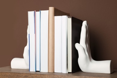 Beautiful hand shaped bookends with books on shelf near brown wall