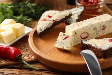 Photo of Tasty butter, dill, chili pepper and rye bread on wooden table, closeup