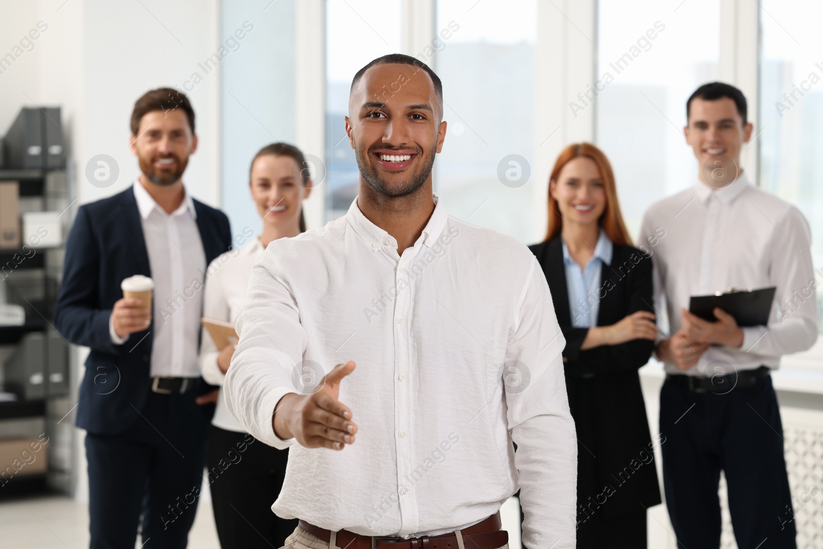 Photo of Group of people in office. Happy man welcoming and offering handshake indoors