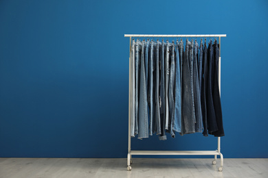 Photo of Rack with stylish jeans near blue wall. Space for text