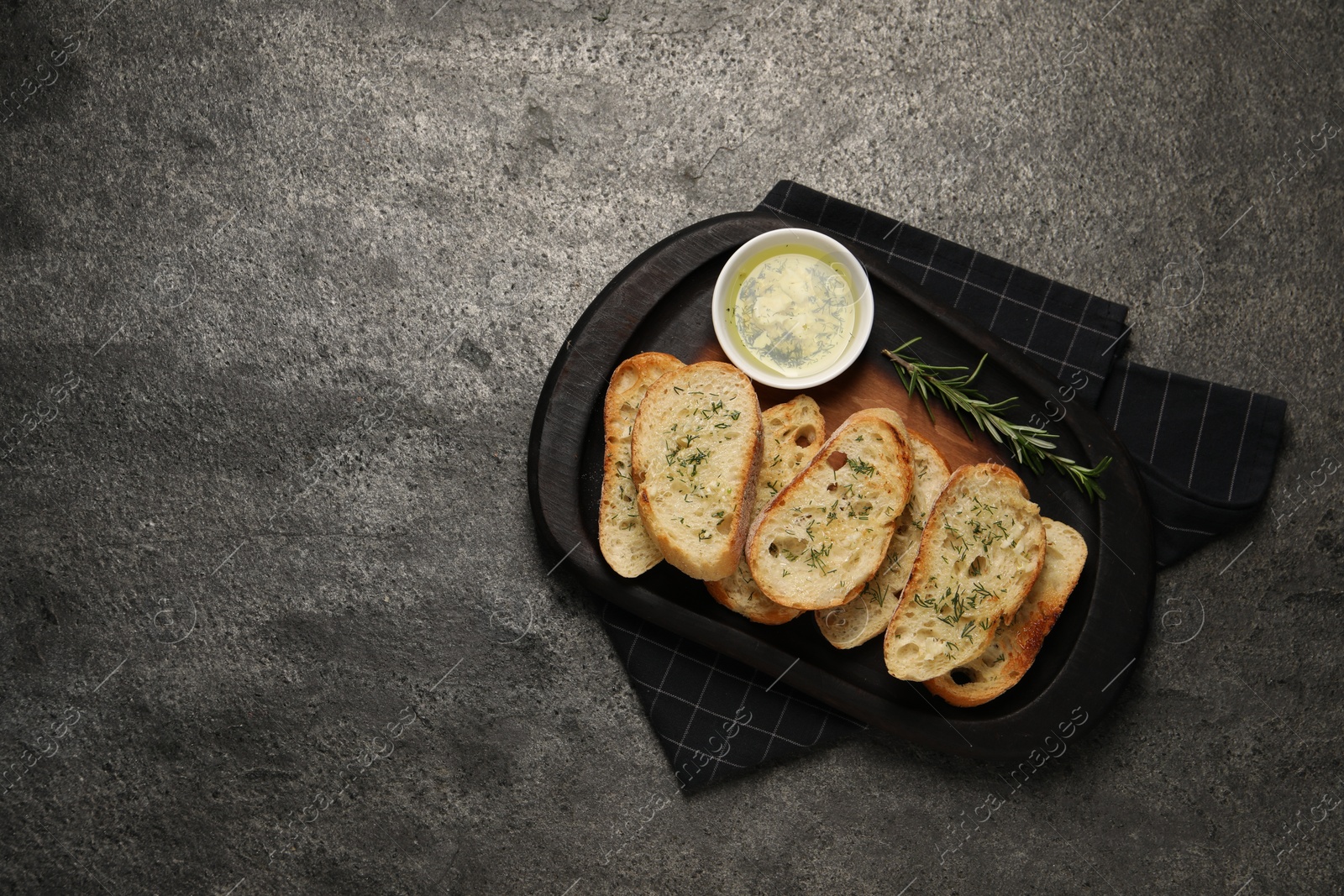 Photo of Tasty baguette with garlic and dill served on grey textured table, top view. Space for text