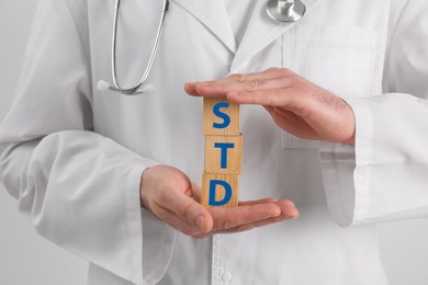 Photo of Doctor holding wooden cubes with abbreviation STD on white background, closeup