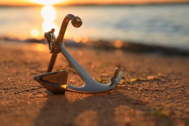 Metal anchor on shore near river at sunset