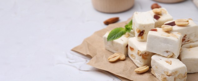 Image of Pieces of delicious nutty nougat on white table, space for text. Banner design