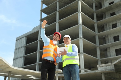Photo of Professional engineer with tablet and foreman in safety equipment at construction site
