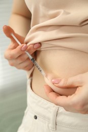 Photo of Diabetes. Woman making insulin injection into her belly indoors, closeup