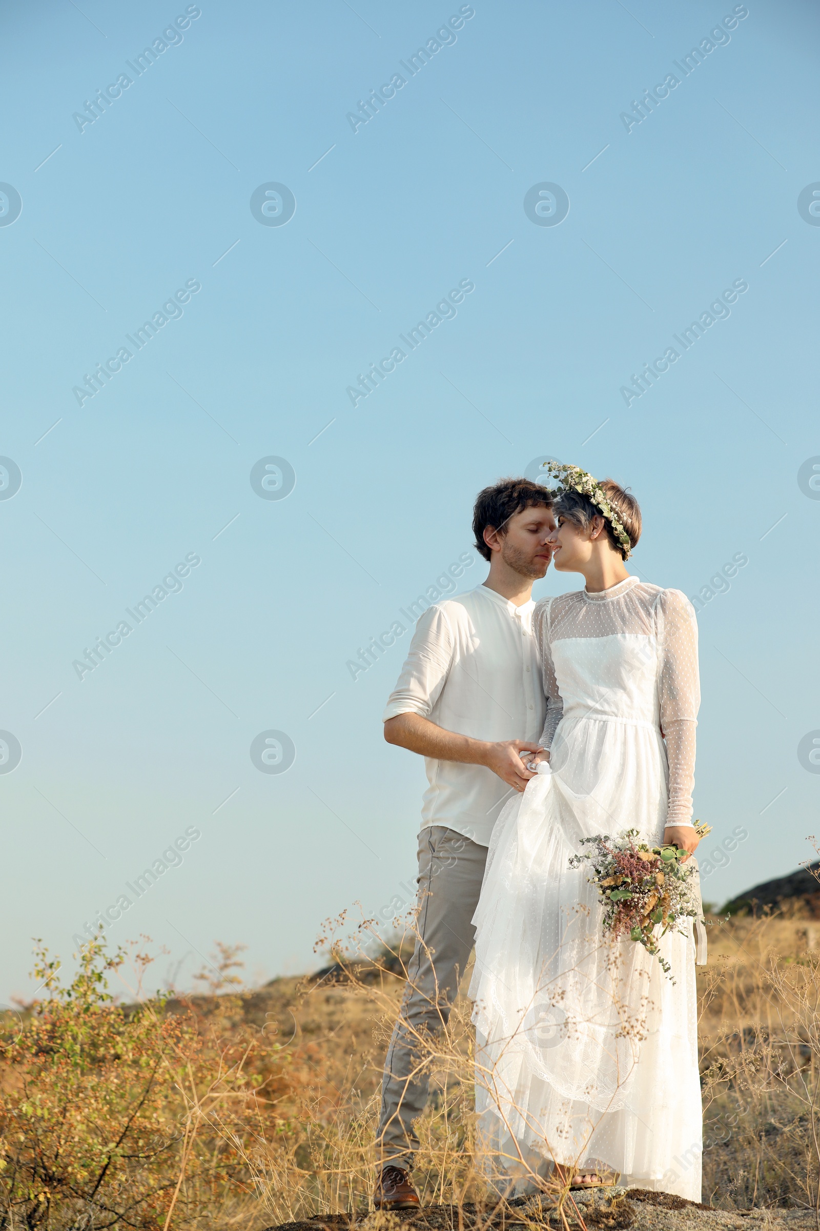 Photo of Happy newlyweds with beautiful field bouquet outdoors