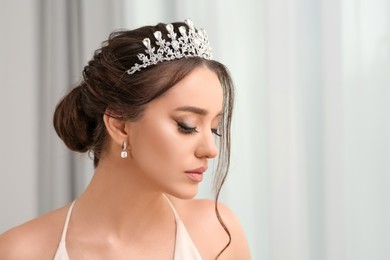 Beautiful young woman wearing luxurious tiara indoors, space for text