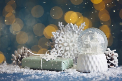 Photo of Beautiful snow globe, gift and decor on blue table against blurred Christmas lights