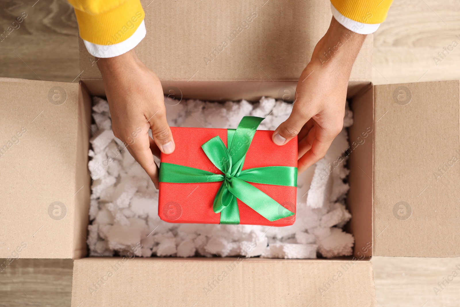 Photo of Man putting Christmas gift box into parcel at wooden table, top view. Sending present by mail