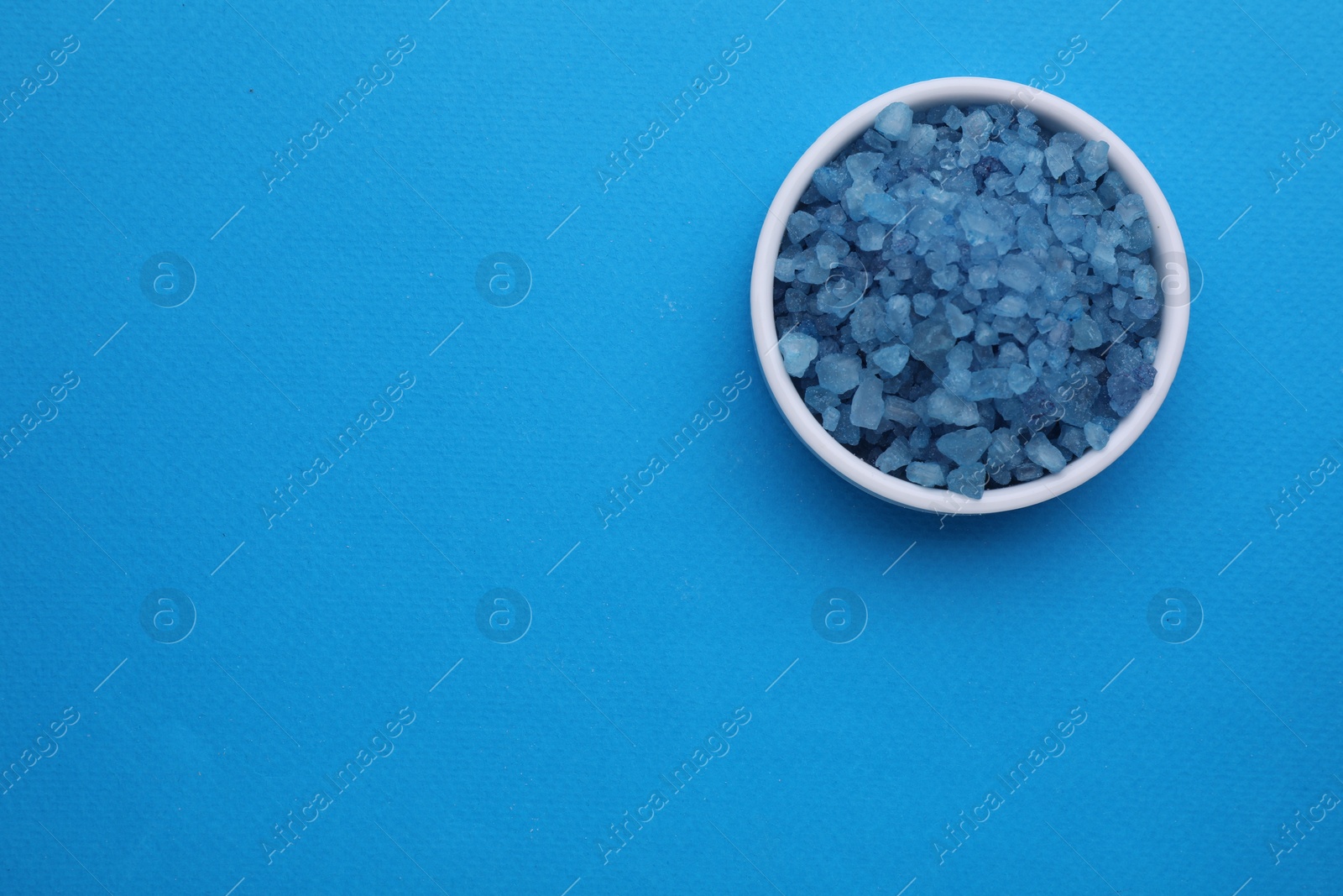 Photo of Bowl with sea salt on light blue background, top view. Space for text