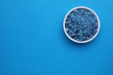 Photo of Bowl with sea salt on light blue background, top view. Space for text