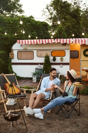 Photo of Happy couple with burgers and beer resting near trailer. Camping season