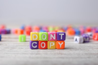 Photo of Colorful cubes with words Don't Copy on white wooden table, closeup. Plagiarism concept