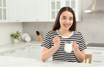 Photo of Portrait of happy woman with tasty yogurt in kitchen. Space for text