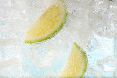 Photo of Juicy lime slices and ice cubes in soda water against light blue background, closeup