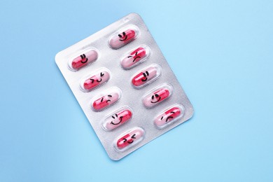 Blister of antidepressant pills with emotional faces on light blue background, top view