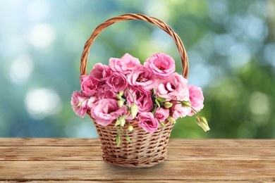 Image of Beautiful pink Eustoma flowers in wicker basket on wooden table outdoors. Bokeh effect