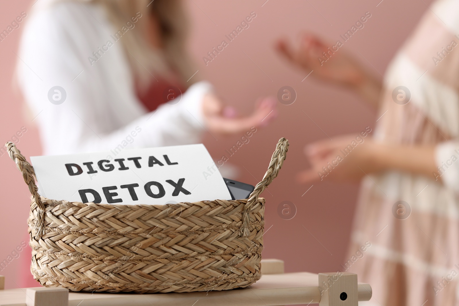 Photo of Women chatting against pink background, focus on wicker basket with sign DIGITAL DETOX