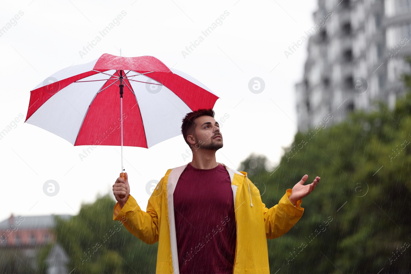 Photo of Handsome young man with bright umbrella outdoors on rainy day