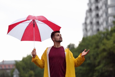 Photo of Handsome young man with bright umbrella outdoors on rainy day