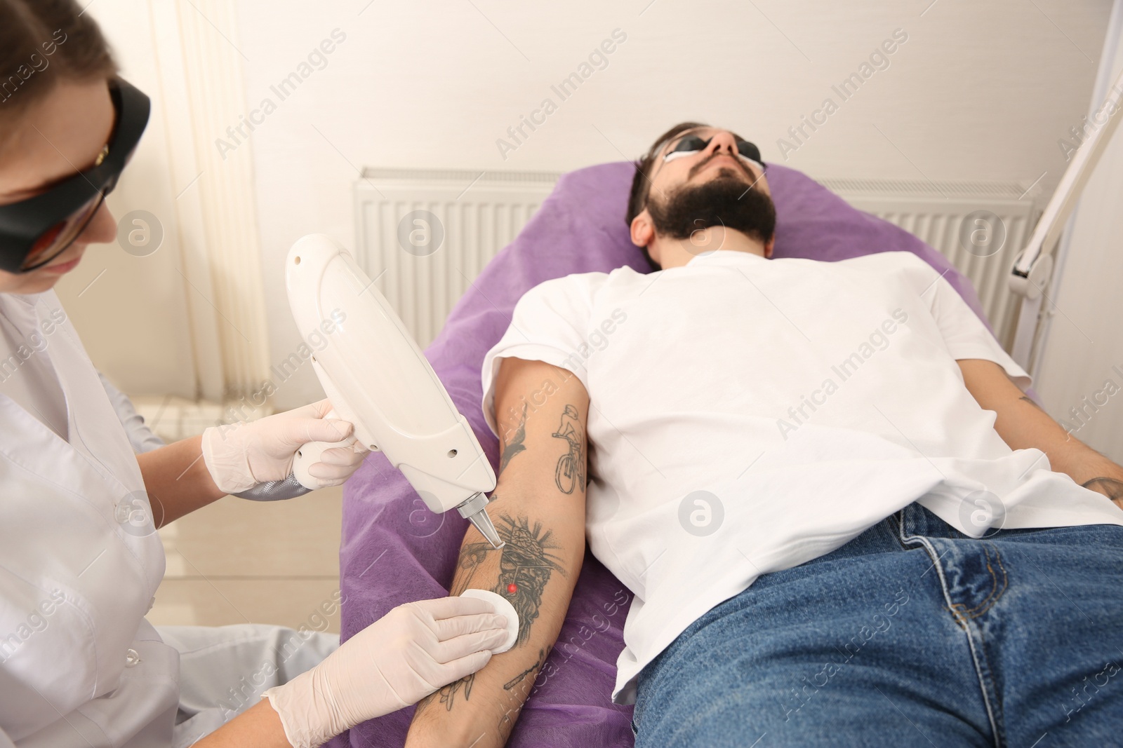 Photo of Young man undergoing laser tattoo removal procedure in salon