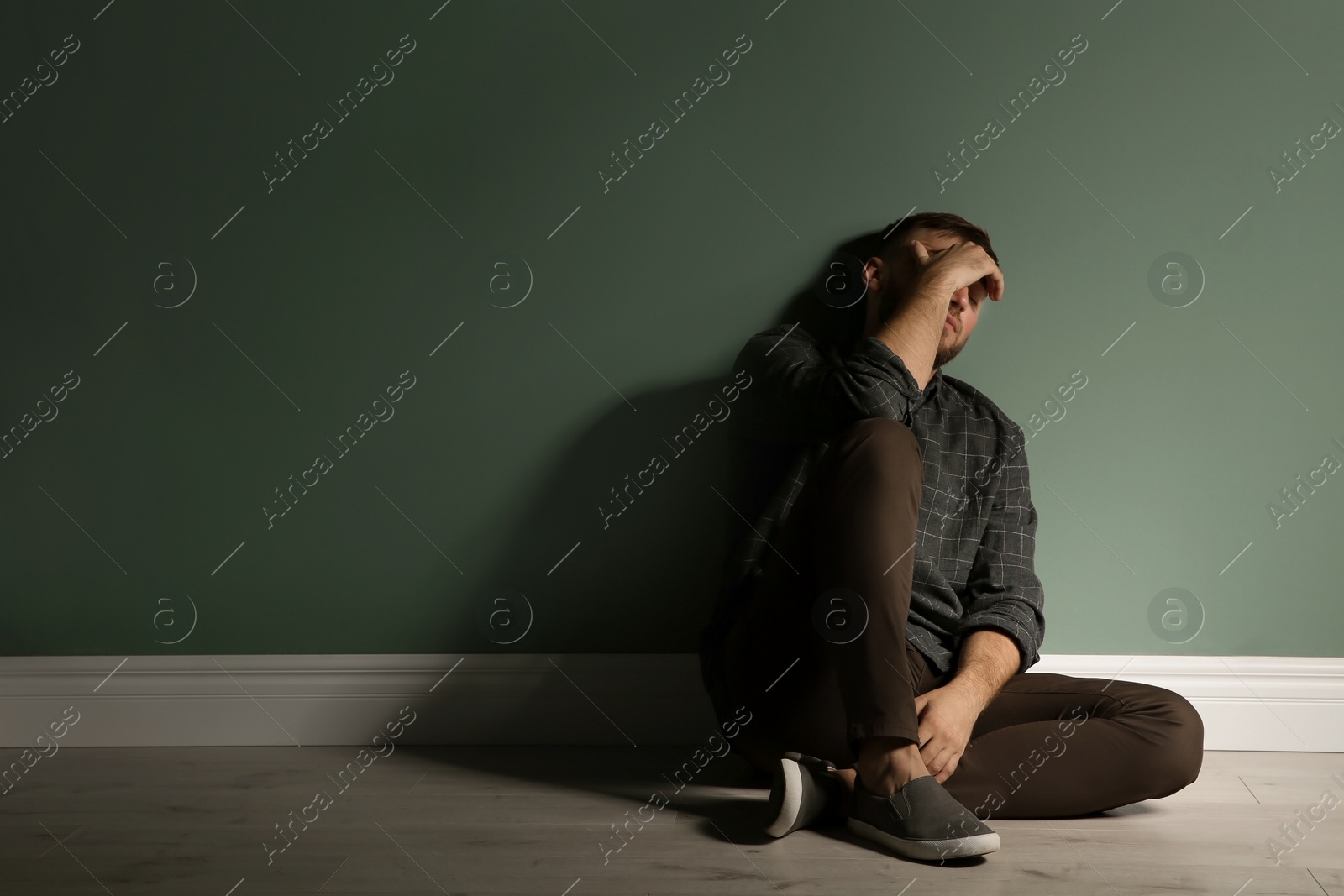 Photo of Depressed young man sitting on floor in darkness