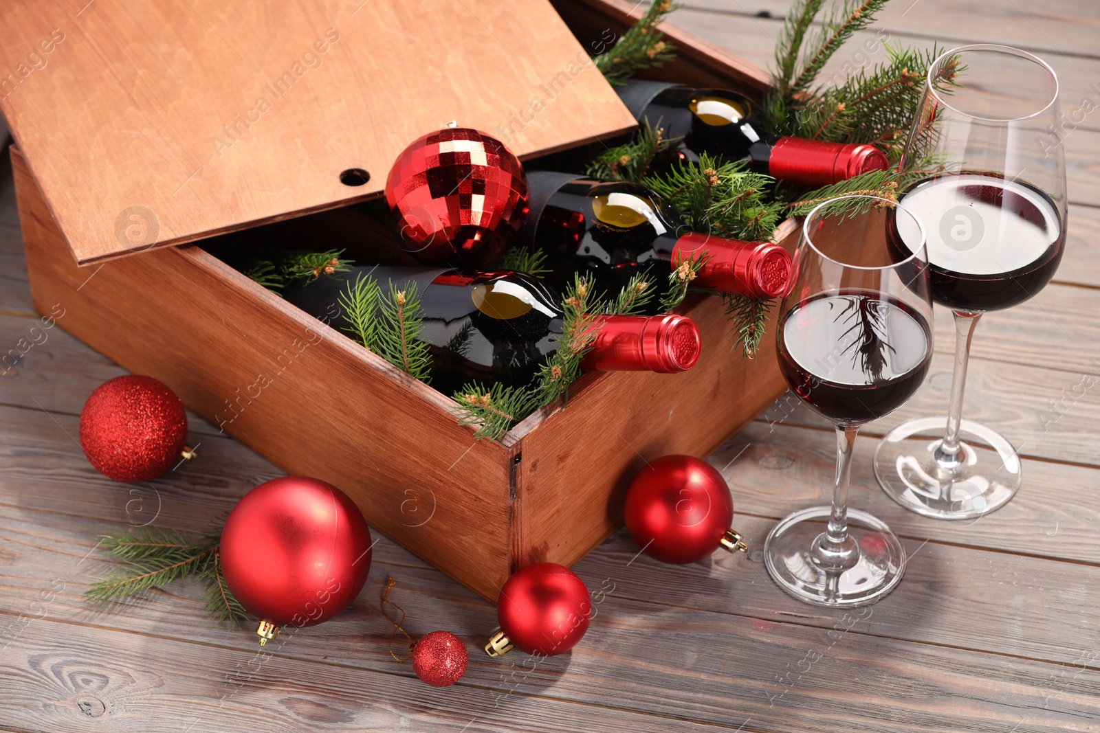 Photo of Wooden crate with bottles of wine, glasses, fir twigs and red Christmas balls on table