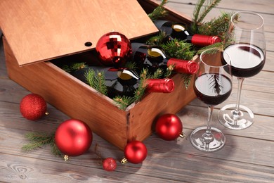 Wooden crate with bottles of wine, glasses, fir twigs and red Christmas balls on table