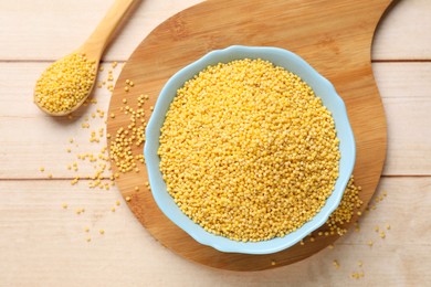 Millet groats in bowl and spoon on light wooden table, flat lay